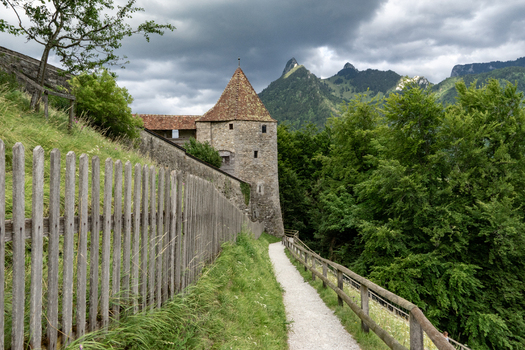 Gruyeres Switzerland 14 May 2026 View of the historic stone fortification tower and castle walls with a wooden fence path and mountain peaks under a cloudy sky. Gruyeres Switzerland 14 May 2026 View of the historic stone fortification tower and castle walls with a wooden fence path and mountain peaks under a cloudy sky.