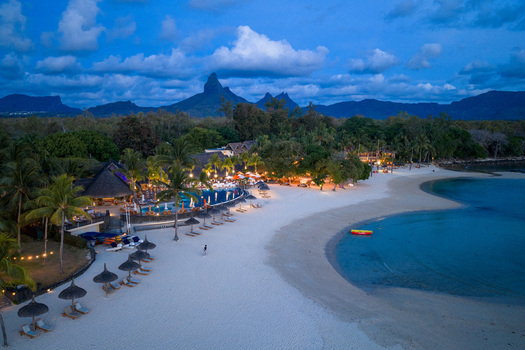 Aerial view of a luxury resort with illuminated pools palm trees and people on a white sand beach at dusk in Mauritius Moka District Mauritius. Aerial view of a luxury resort with illuminated pools palm trees and people on a white sand beach at dusk in Mauritius Moka District Mauritius.