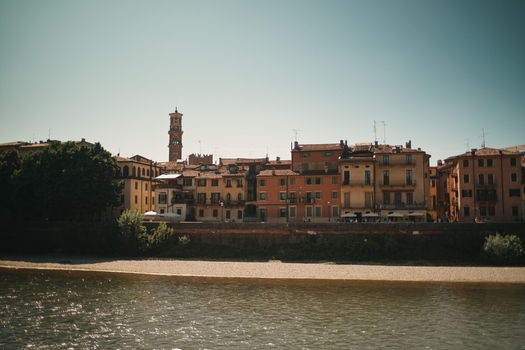 View of historic colorful buildings along the Adige river with the Lamberti Tower rising above the skyline in Verona Veneto Italy.