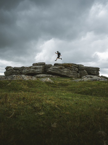 View of a man jumping on rugged rocks under a cloudy sky Dartmoor National Park Devon Great Britain.