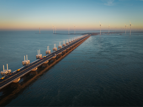 Aerial view of Deltawerken storm surge barrier with wind turbines and a road during golden hour in Netherlands.