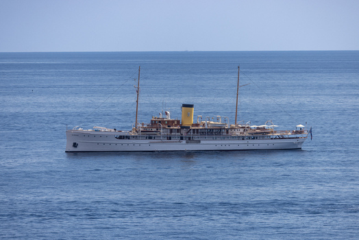Aerial view of a classic white yacht with a yellow funnel sailing on the blue Mediterranean Sea off the coast of Monaco Monaco.