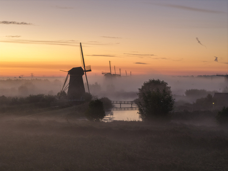 Aerial view of UNESCO World Heritage Kinderdijk windmills shrouded in thick morning mist during a vibrant sunrise Kinderdijk Zuid Holland Netherlands.