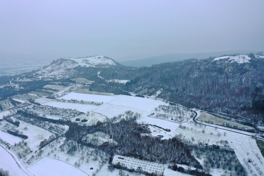 Aerial view of Walberla hill surrounded by snow covered fields and forests under a misty winter sky Kirchehrenbach Bavaria Germany.