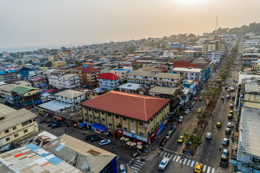 Aerial view of the dense urban landscape with colorful rooftops busy streets with yellow taxis and the coastline under a hazy sky in Monrovia Montserrado Liberia. Aerial view of the dense urban landscape with colorful rooftops busy streets with yellow taxis and the coastline under a hazy sky in Monrovia Montserrado Liberia.