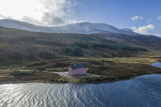 Aerial view of The Pink House on the shore of Loch Glass with snow capped mountains and rugged terrain in Dingwall Scotland United Kingdom. Aerial view of The Pink House on the shore of Loch Glass with snow capped mountains and rugged terrain in Dingwall Scotland United Kingdom.