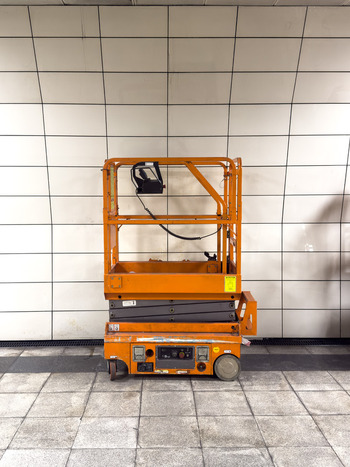 View of an orange scissor lift parked against a white tiled wall in a subway station in Istanbul Istanbul Turkiye.