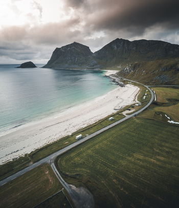 Aerial view of Vik Strand featuring a white sand beach turquoise sea dramatic mountains and a coastal road winding through green fields in Leknes Nordland Norway.
