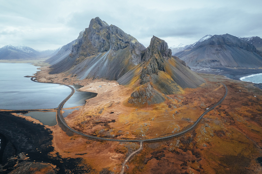 Aerial view of Hvalnes Nature Reserve Beach and the jagged peaks of the mountain with a winding coastal road and black sand at Eystrahorn Sveitarfelagid Hornafjordur Iceland. Aerial view of Hvalnes Nature Reserve Beach and the jagged peaks of the mountain with a winding coastal road and black sand at Eystrahorn Sveitarfelagid Hornafjordur Iceland.