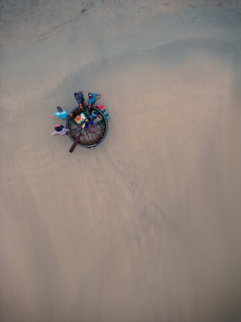 Aerial view of a traditional Vietnamese basket boat with fishermen standing on the wet sand of a beach in Vietnam. Aerial view of a traditional Vietnamese basket boat with fishermen standing on the wet sand of a beach in Vietnam.