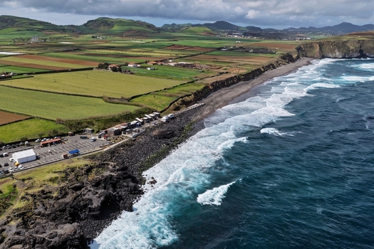 Aerial view of Praia do Areal de Santa Barbara with dark volcanic sand crashing Atlantic waves and lush green fields in Ribeira Grande Acores Portugal. Aerial view of Praia do Areal de Santa Barbara with dark volcanic sand crashing Atlantic waves and lush green fields in Ribeira Grande Acores Portugal.