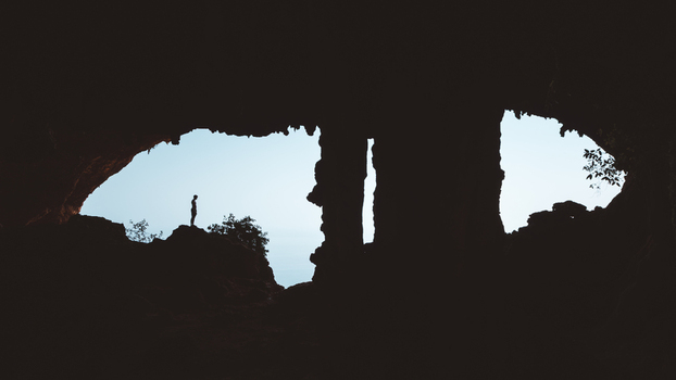 View of a person silhouetted against the bright opening of Hoq Cave with rugged rock formations and natural light filtering through the entrance in Socotra Socotra Yemen. View of a person silhouetted against the bright opening of Hoq Cave with rugged rock formations and natural light filtering through the entrance in Socotra Socotra Yemen.