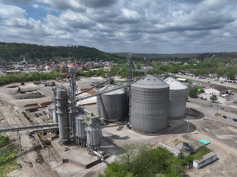 Aerial view of large industrial grain silos and metal elevators surrounded by green trees and a small town under a cloudy sky Aurora Indiana United States. Aerial view of large industrial grain silos and metal elevators surrounded by green trees and a small town under a cloudy sky Aurora Indiana United States.
