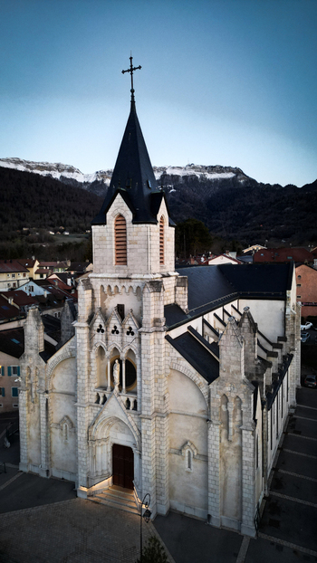Aerial view of Eglise Saint Pierre with its tall spire and stone architecture against the backdrop of mountains and a clear blue sky in Gex Auvergne Rhone Alpes France. Aerial view of Eglise Saint Pierre with its tall spire and stone architecture against the backdrop of mountains and a clear blue sky in Gex Auvergne Rhone Alpes France.
