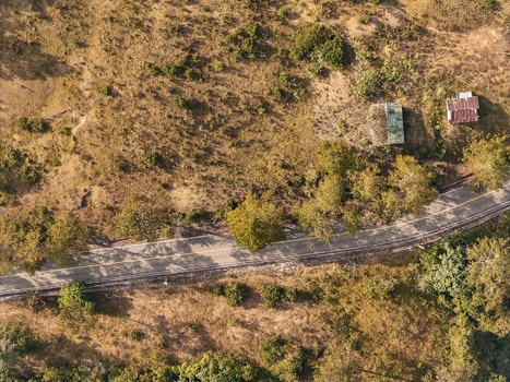 Aerial view of a winding road cutting through dry grassy hills with scattered trees and small rustic buildings in Jarabacoa La Vega Province Dominican Republic.