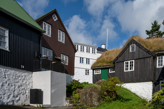 View of traditional Faroese houses with iconic grass roofs black wooden siding and white stone foundations under a bright blue sky in the Faroe Islands. View of traditional Faroese houses with iconic grass roofs black wooden siding and white stone foundations under a bright blue sky in the Faroe Islands.