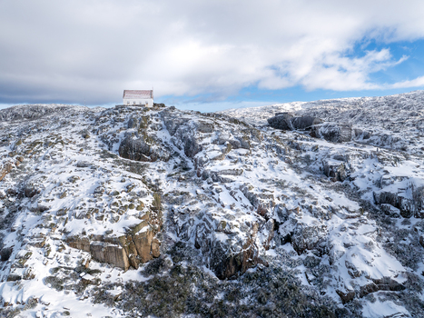 Aerial view of a snow dusted rocky peak crowned with a solitary building under a bright sky Lagoa Comprida São Romão Serra da Estrella Portugal. Aerial view of a snow dusted rocky peak crowned with a solitary building under a bright sky Lagoa Comprida São Romão Serra da Estrella Portugal.
