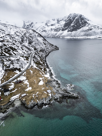 Aerial view of Grotfjord with a winding coastal road snow covered mountains and turquoise water in Tromvik Troms Norway. Aerial view of Grotfjord with a winding coastal road snow covered mountains and turquoise water in Tromvik Troms Norway.
