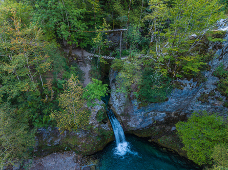 Aerial view of Blue Eye Theth a natural spring with turquoise water flowing into a pool surrounded by lush forest rocky cliffs and a wooden footbridge Theth Shkoder County Albania. Aerial view of Blue Eye Theth a natural spring with turquoise water flowing into a pool surrounded by lush forest rocky cliffs and a wooden footbridge Theth Shkoder County Albania.
