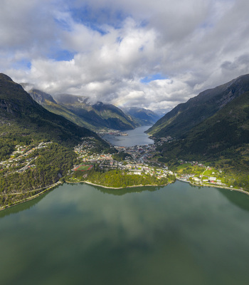 Aerial view of the town of Odda nestled between steep mountains and the calm waters of the fjord under a cloudy sky Odda Vestland Norway. Aerial view of the town of Odda nestled between steep mountains and the calm waters of the fjord under a cloudy sky Odda Vestland Norway.