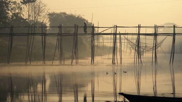 View of a person walking on a bamboo bridge at dawn Bangladesh.