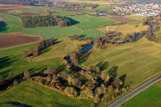 Aerial view of the winding Aisch river flowing through the Aischtalweg valley with green meadows and autumn trees near Uehlfeld Bayern Germany. Aerial view of the winding Aisch river flowing through the Aischtalweg valley with green meadows and autumn trees near Uehlfeld Bayern Germany.