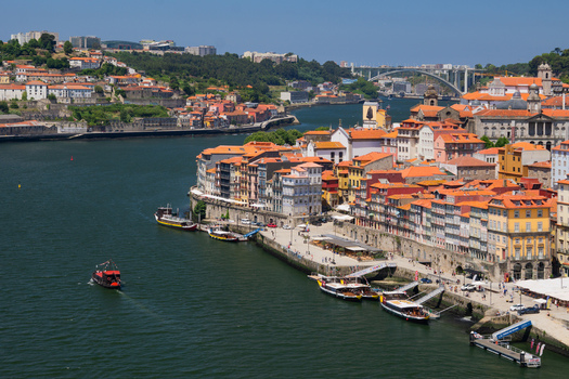 Aerial view of the Douro River snaking through the city lined with colorful buildings and boats under a vast sky Porto Porto District Portugal. Aerial view of the Douro River snaking through the city lined with colorful buildings and boats under a vast sky Porto Porto District Portugal.