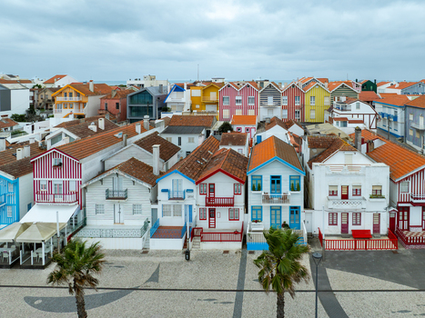 Aerial view of vibrantly striped houses stand side by side creating a stunning contrast against the grey skies and sandy terrain Costa Nova Aveiro Portugal.