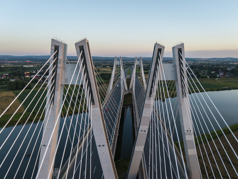 Aerial view of the Most na S7 cable stayed bridge with its distinctive V shaped pylons spanning the river surrounded by green fields and highway infrastructure in Krakow Malopolskie Poland. Aerial view of the Most na S7 cable stayed bridge with its distinctive V shaped pylons spanning the river surrounded by green fields and highway infrastructure in Krakow Malopolskie Poland.