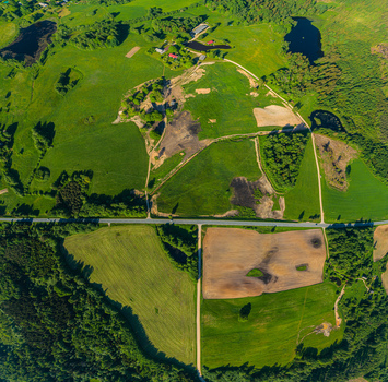 Aerial view of lush green agricultural fields patches of bare soil and a rural road winding through the countryside in Latvia. Aerial view of lush green agricultural fields patches of bare soil and a rural road winding through the countryside in Latvia.
