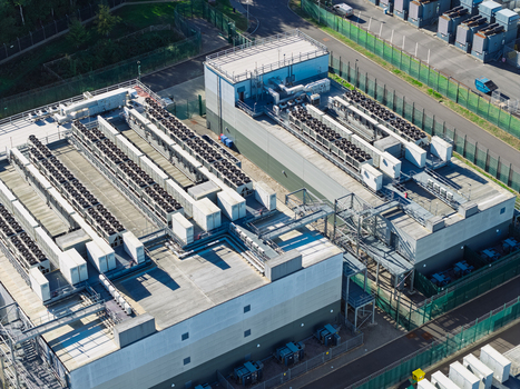 Aerial view of a large data center facility with rows of cooling units on the roof industrial infrastructure and a fenced perimeter in the United Kingdom.