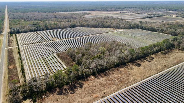 Aerial view of a vast solar farm gleaming under the sun s glare contrasting with the surrounding dark green forest Elkton Florida United States. Aerial view of a vast solar farm gleaming under the sun s glare contrasting with the surrounding dark green forest Elkton Florida United States.
