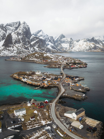 Aerial view of a road connecting islands with vibrant turquoise waters and snow capped mountains in the distance Sakrisøya Nordland Norway. Aerial view of a road connecting islands with vibrant turquoise waters and snow capped mountains in the distance Sakrisøya Nordland Norway.