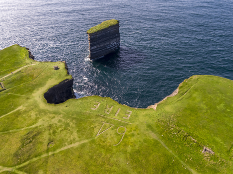 Aerial view of Dun Briste Sea Stack rising from the Atlantic Ocean near grassy cliffs with the historic EIRE 64 sign visible in County Mayo Ireland. Aerial view of Dun Briste Sea Stack rising from the Atlantic Ocean near grassy cliffs with the historic EIRE 64 sign visible in County Mayo Ireland.