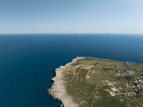 Aerial view of the rugged coastline of the Plemmirio Marine Protected Area with rocky cliffs and scattered houses under a clear blue sky in Plemmirio Sicily Italy. Aerial view of the rugged coastline of the Plemmirio Marine Protected Area with rocky cliffs and scattered houses under a clear blue sky in Plemmirio Sicily Italy.