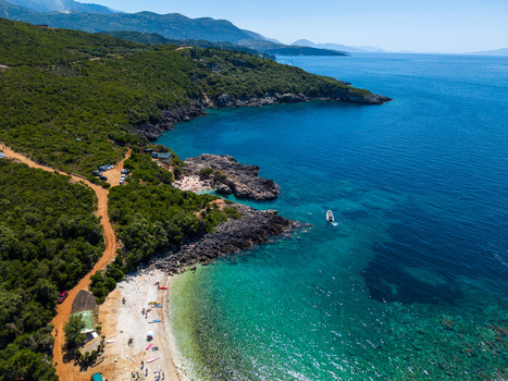 Aerial view of Aquarium Beach with turquoise water rocky cliffs and lush green hills in Jala Vlore County Albania.