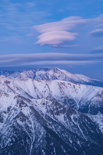 Aerial view of the snow covered peaks of the High Tatras mountains under unique lenticular clouds in the sky in Vysoke Tatry Presov Region Slovakia.