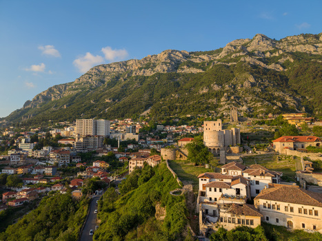 Aerial view of the historic Kruje Castle and traditional red tiled houses nestled against the rugged mountain slopes under a clear blue sky in Kruje Durres County Albania.