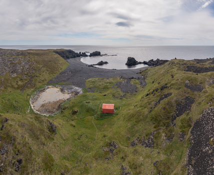 Aerial view of the black sand beach at Djupalonssandur with a small red building set against rugged volcanic terrain and the Atlantic Ocean in Iceland. Aerial view of the black sand beach at Djupalonssandur with a small red building set against rugged volcanic terrain and the Atlantic Ocean in Iceland.