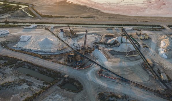 Aerial view of an industrial sea salt processing facility with conveyor belt systems heavy machinery and large white salt piles in Aigues Mortes Occitanie France.