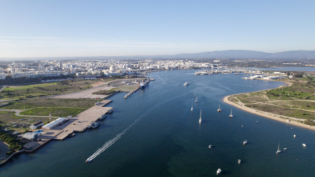 Aerial view of the Ferragudo harbor and river estuary with boats sailing on the water coastal town buildings and distant hills in Ferragudo Faro District Portugal.