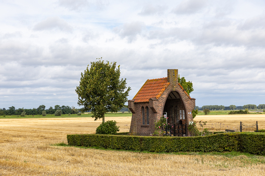 View of Kapel op De Heuvel surrounded by a green hedge and a harvested field under a cloudy sky in Bemmel Gelderland Netherlands. View of Kapel op De Heuvel surrounded by a green hedge and a harvested field under a cloudy sky in Bemmel Gelderland Netherlands.