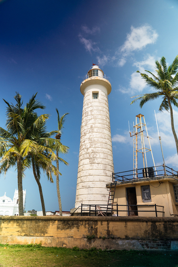 View of Galle Lighthouse surrounded by palm trees under a bright blue sky Galle Southern Province Sri Lanka.