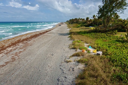 Aerial view of the beach where the turquoise ocean meets the sandy shore fringed by vibrant green vegetation under a partly cloudy sky Jupiter Island Florida United States. Aerial view of the beach where the turquoise ocean meets the sandy shore fringed by vibrant green vegetation under a partly cloudy sky Jupiter Island Florida United States.
