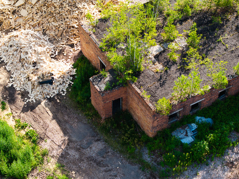 Aerial view of an abandoned brick building with trees growing on its roof and large piles of wood chips nearby in Salgale parish Jelgava Municipality Latvia. Aerial view of an abandoned brick building with trees growing on its roof and large piles of wood chips nearby in Salgale parish Jelgava Municipality Latvia.