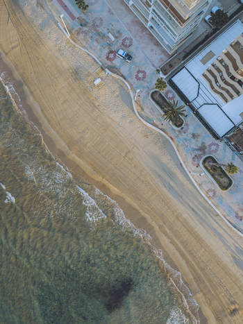 Aerial view of a sandy beach meeting a patterned promenade with palm trees and modern buildings in Calp Valencian Community Spain. Aerial view of a sandy beach meeting a patterned promenade with palm trees and modern buildings in Calp Valencian Community Spain.