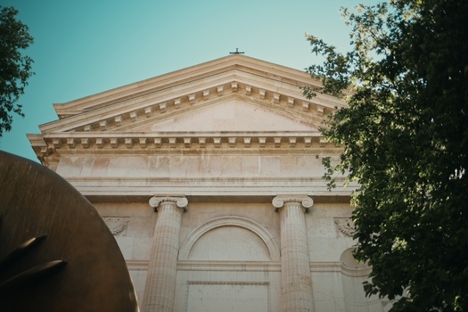 View of the neoclassical facade of a historic building with Ionic columns and a pediment framed by green trees under a clear sky in Verona Veneto Italy.