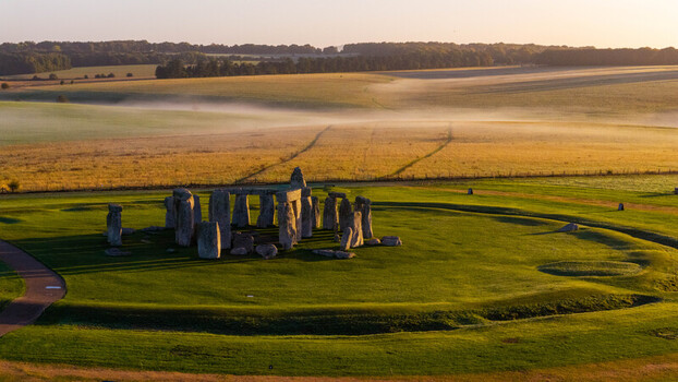Aerial view of Stonehenge surrounded by lush green fields and morning mist under golden hour light in Salisbury England United Kingdom. Aerial view of Stonehenge surrounded by lush green fields and morning mist under golden hour light in Salisbury England United Kingdom.