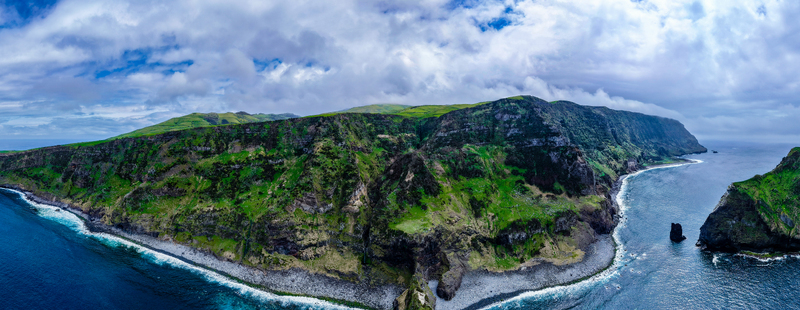 Aerial view of rugged cliffs meet the turquoise sea lush green vegetation blankets the landscape under a sky of scattered clouds Flores A&ccedil;ores Portugal.