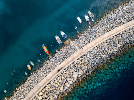 Aerial view of boats bobbing gently on the azure waters beside the rugged rocky breakwater of Mgarr Harbour Gozo Malta. Aerial view of boats bobbing gently on the azure waters beside the rugged rocky breakwater of Mgarr Harbour Gozo Malta.